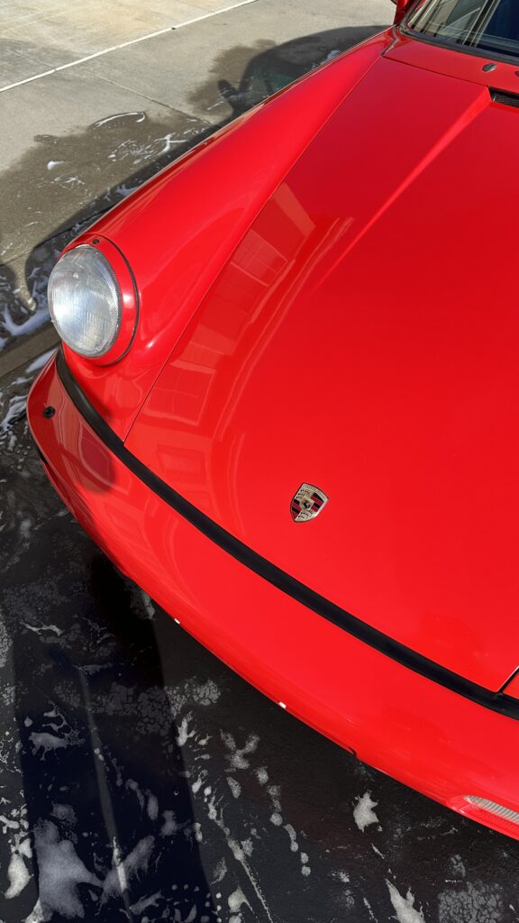 Red Porsche 911 covered in wash foam during a clay and seal service