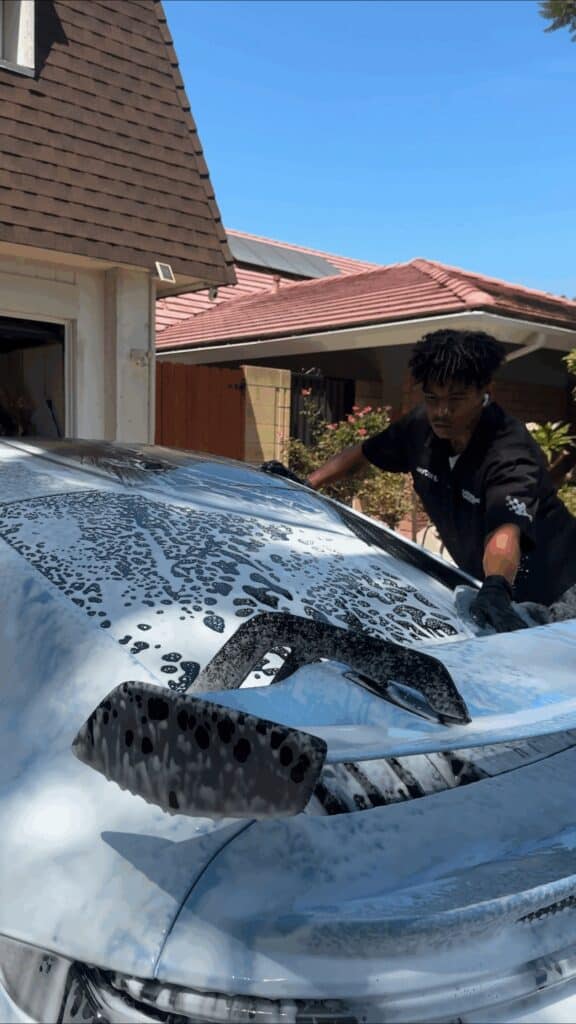 Detailer hand washing a foam covered Porsche 911 GT3 on site