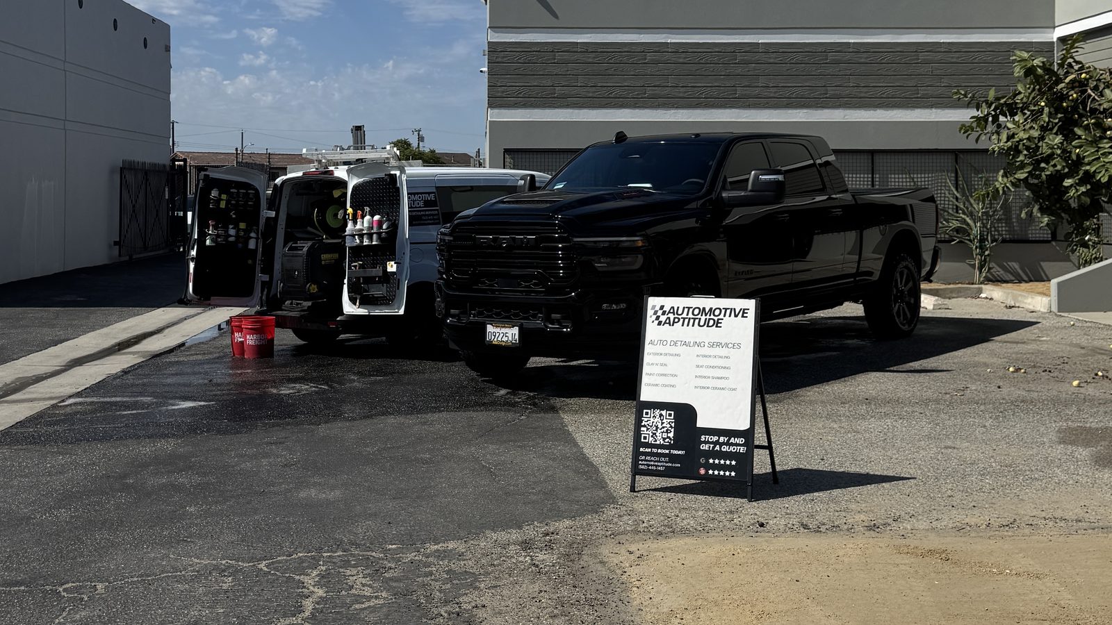 The Automotive Aptitude van parked with its doors open beside a black Ram truck, shelves of detailing product inside
