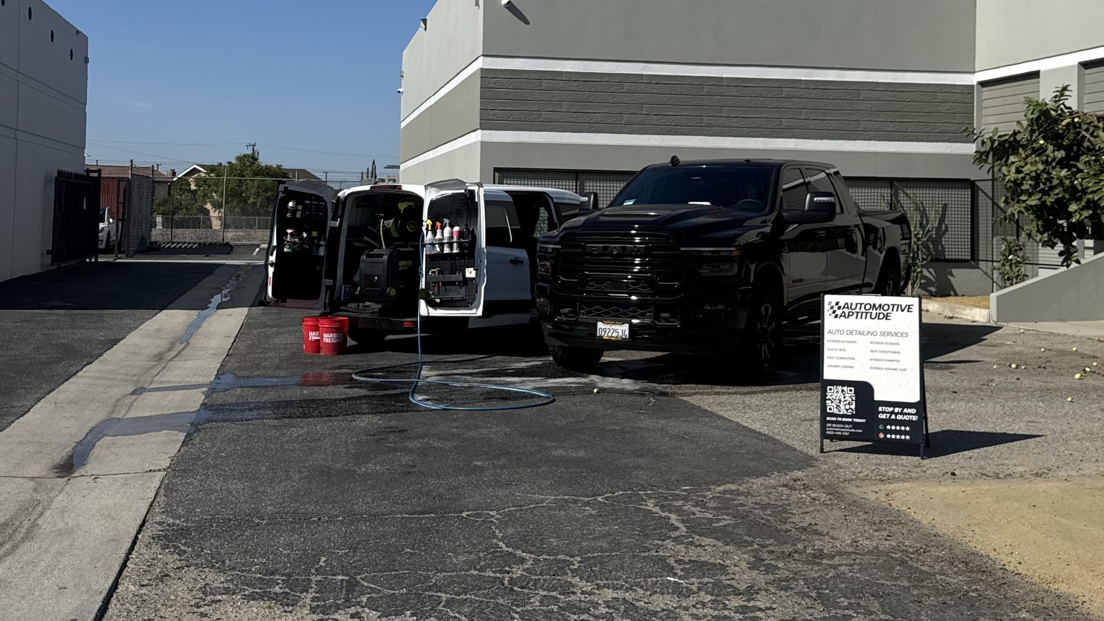 Detailing van and black Ram truck on a job, hose run out across the lot